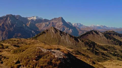 Alpine mountain range with rugged peaks and grassy hills under a clear blue sky Stock Footage 339780101