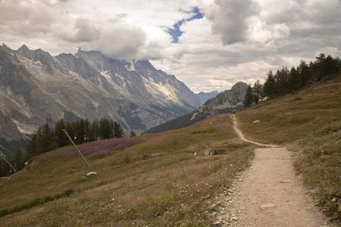 Alpine mountain trail winding through valley with hiker Stock Photos