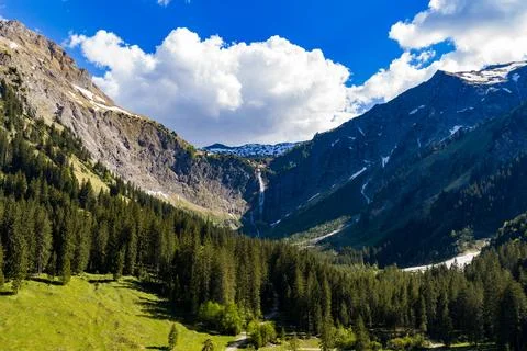 Alpine Mountain Valley With Pine Forest, Waterfall and Snow-Capped Peaks Un.. Stock Photos