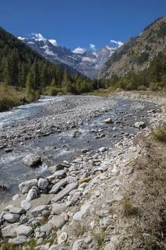 Alpine river flowing through a valley with snowy mountains Stock Photos
