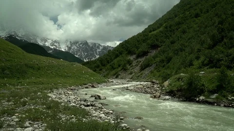 Alpine river. Snow capped mountain peaks and clouds in the background. Summer Stock Footage 115963105