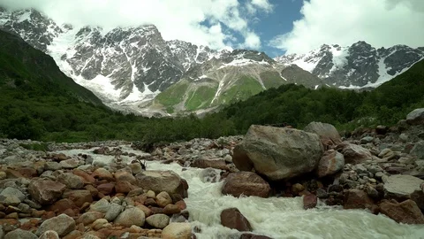 Alpine river. Snow capped mountain peaks and clouds in the background. Summer Stock Footage 115963121