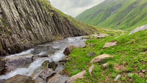 Alpine stream flows beside layered rock formations in the Chaukhi region Stock Footage 340388252