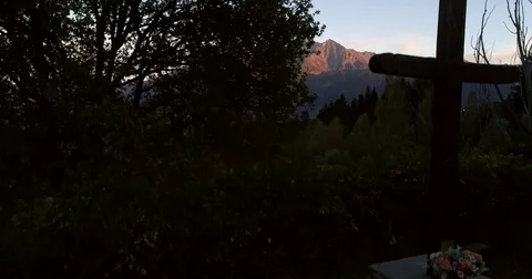 Alpine sunset, Cinema 4k rising view behind a grave cross, revealing mountain Stock Footage 84001955