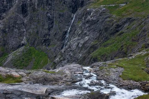 Alpine valley in Norway with cascading stream, dark slate cliffs, green veget Stock Photos