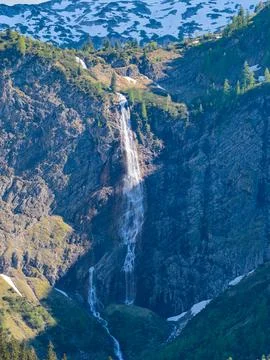 Alpine Waterfall Cascading Down Rocky Mountain Cliff With Snow Patches And .. Foto stock