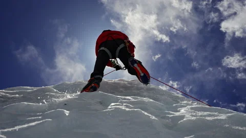 Alpinist equipped with red crampon climb over ice wall under blue sunny sky Stock Footage