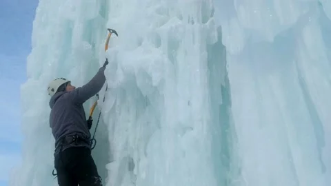 Alpinist man with ice tools axe climbing a large wall of ice Stock Footage 139290573