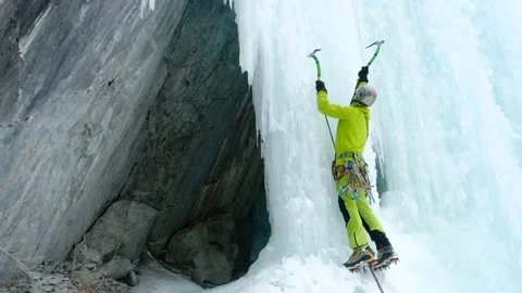 Alpinist man with ice tools axe climbing a frozen waterfall, a large wall of ice Stock Footage 143047890