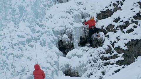 Alpinist man with ice tools axe climbing a frozen waterfall, a large wall of ice Stock Footage 143047994