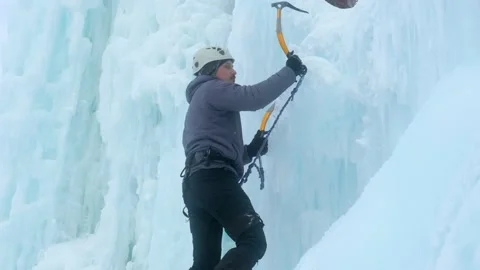 Alpinist man with ice tools axe climbing a large wall of ice. Stock Footage 155871737