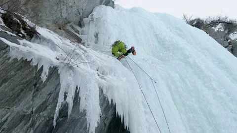 Alpinist man with ice tools axe climbing a frozen waterfall, a large wall of ice Stock Footage 160234523