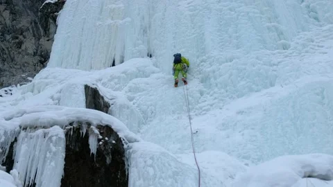 Alpinist man with ice tools axe climbing a frozen waterfall, a large wall of ice Stock Footage 164884563