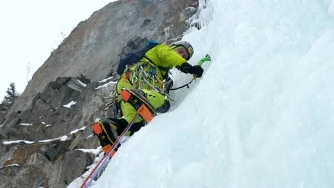 Alpinist man with ice tools axe climbing a frozen waterfall, a large wall of ice Stock Footage 164884692