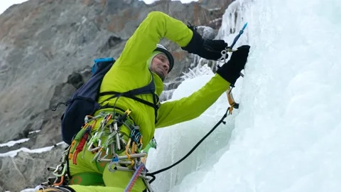 Alpinist man with ice tools axe climbing a frozen waterfall, a large wall of ice Stock Footage 164884725