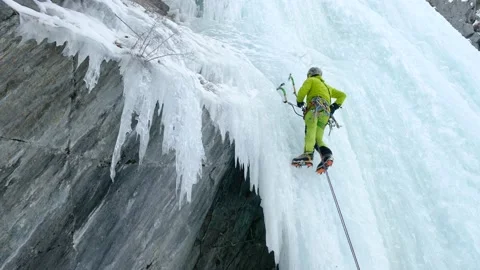 Alpinist man with ice tools axe climbing a frozen waterfall, a large wall of ice Stock Footage 164884760