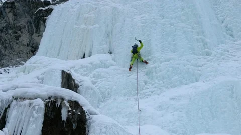 Alpinist man with ice tools axe climbing a frozen waterfall, a large wall of ice Stock Footage 165190926
