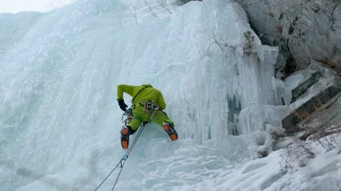 Alpinist man with ice tools axe climbing a frozen waterfall, a large wall of ice Stock Footage 165190966