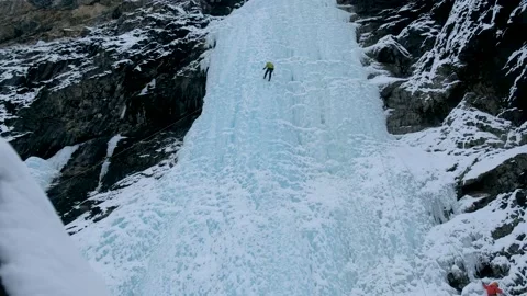 Alpinist man with ice tools axe climbing a frozen waterfall, a large wall of ice Stock Footage 165191077