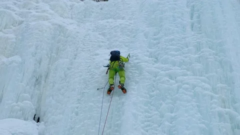 Alpinist man with ice tools axe climbing a frozen waterfall, a large wall of ice Stock Footage 166130835