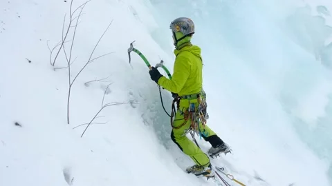 Alpinist man with ice tools axe climbing a frozen waterfall, a large wall of ice Stock Footage 169028230