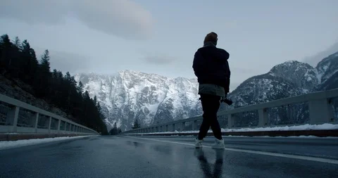 An alternative girl with a camera standing in the middle of an alpine road with  Video stock 129396971