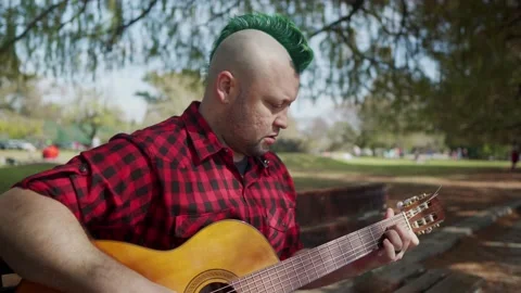 An alternative man concentrated while playing guitar at park Stock-Footage 139273963