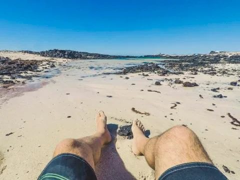 Alternative point of view of man legs at the beach with swimwear enjoying the Stock Photos