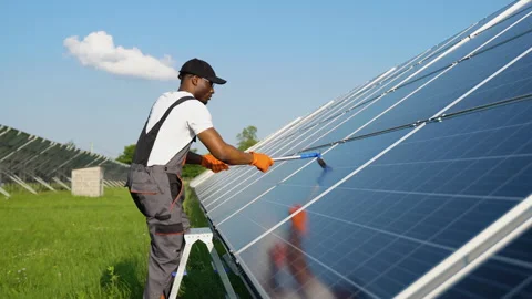 Alternative power plant worker in uniform cleaning solar panels with mop Stock Footage 246803149
