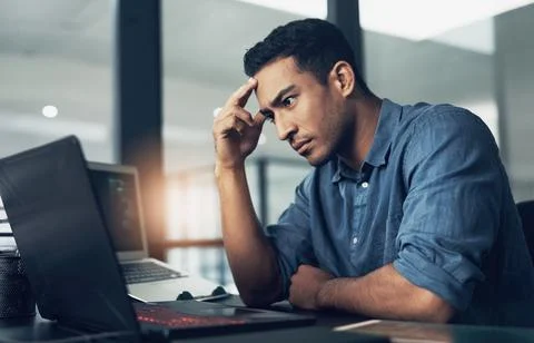 Am I reaping my karma. a stressed young man using a laptop in a modern office. Stock Photos