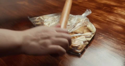 Amaretti in a plastic bag being crushed with a rolling pin. Видео 330134051