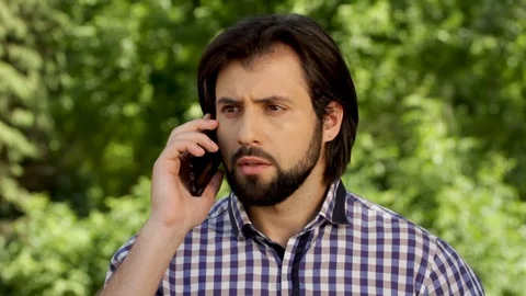 Amazed and distracted man us talking on the phone. He has a quarrel. Guy is Stock Footage 99740182