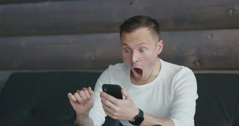 Amazed man receives joyful message on the phone. Happy person reads good news on Stock Footage 197816543