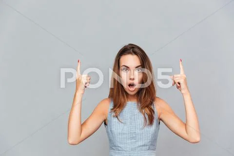 Amazed shocked young woman pointing up with both hands Stock Photos