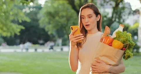 Amazed woman smiling while standing and holding bag with food and phone. Girl Stock Footage 129660552