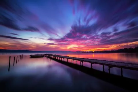Amazing colorful sunset view at a lake coast with boat and wooden pier Stock Photos