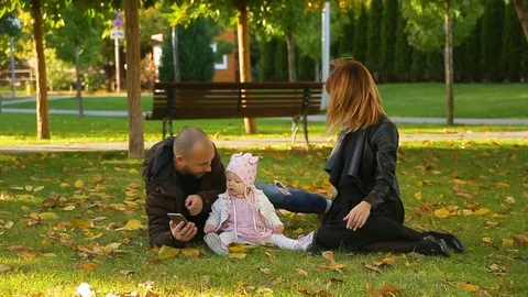 Amazing couple and daughter sit on grass in park with yellow leaves in autumn Stock Footage 112321663