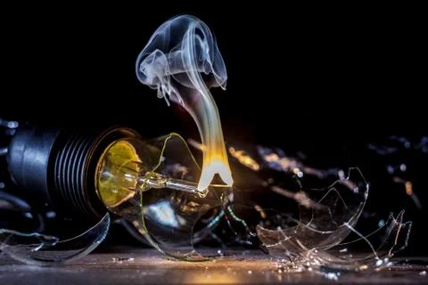 Amazing explosion of a burning light bulb with splinters and smoke on a black Stock Photos