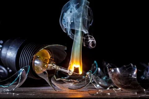 Amazing explosion of a burning light bulb with splinters and smoke on a black Stock Photos
