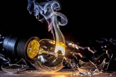 Amazing explosion of a burning light bulb with splinters and smoke on a black Stock Photos