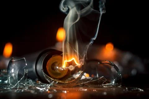 Amazing explosion of a burning light bulb with splinters and smoke on a black Stock Photos