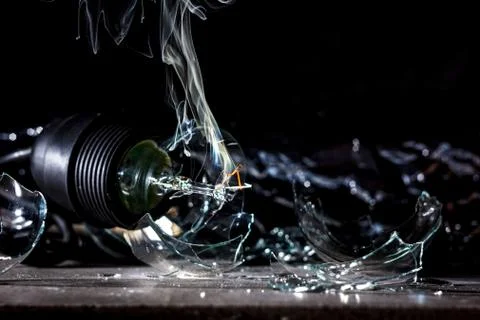 Amazing explosion of a burning light bulb with splinters and smoke on a black Stock Photos