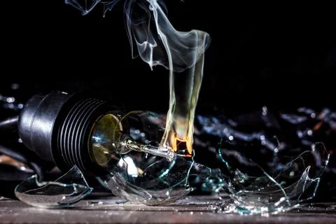 Amazing explosion of a burning light bulb with splinters and smoke on a black Stock Photos