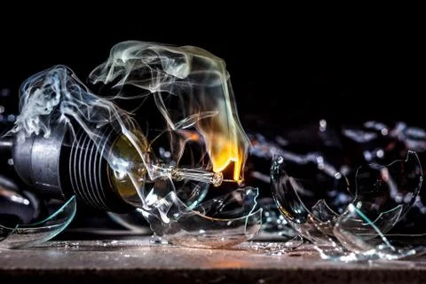 Amazing explosion of a burning light bulb with splinters and smoke on a black Stock Photos