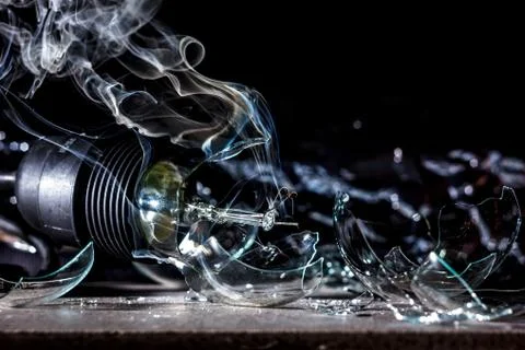 Amazing explosion of a burning light bulb with splinters and smoke on a black Stock Photos