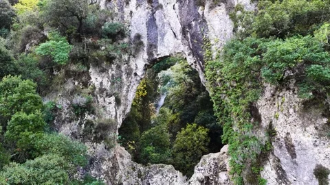 Amazing natural rock arch window framing a lush green forest and waterfall Stock Footage 321790997