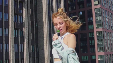 Amazing Red-Haired model suck lollipop on rooftop, enjoying view over city Stock Footage 160558634