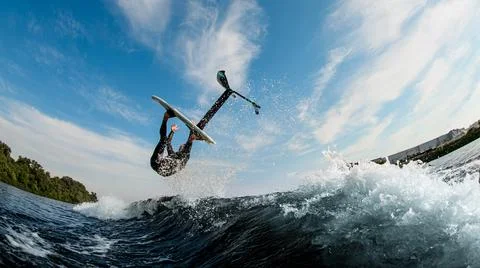 Amazing view of man effectively performs trick over the wave with foilboard Fotos Stock