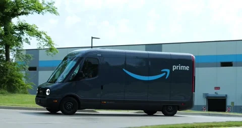 Amazon EV vans drive out of warehouse, made by Rivian, electric vehicles, Stock Footage 338194717