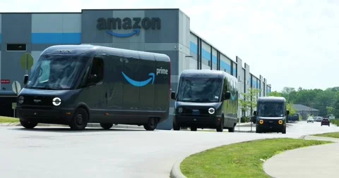 Amazon EV vans drive out of warehouse, made by Rivian, electric vehicles, Stock Footage 338194757